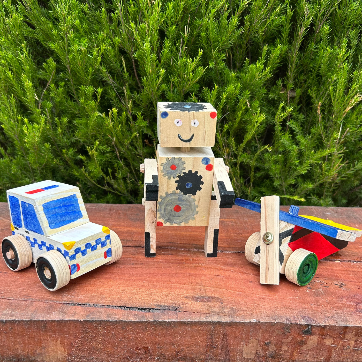 Wooden toy robot and cars on a wooden surface with green foliage in the background