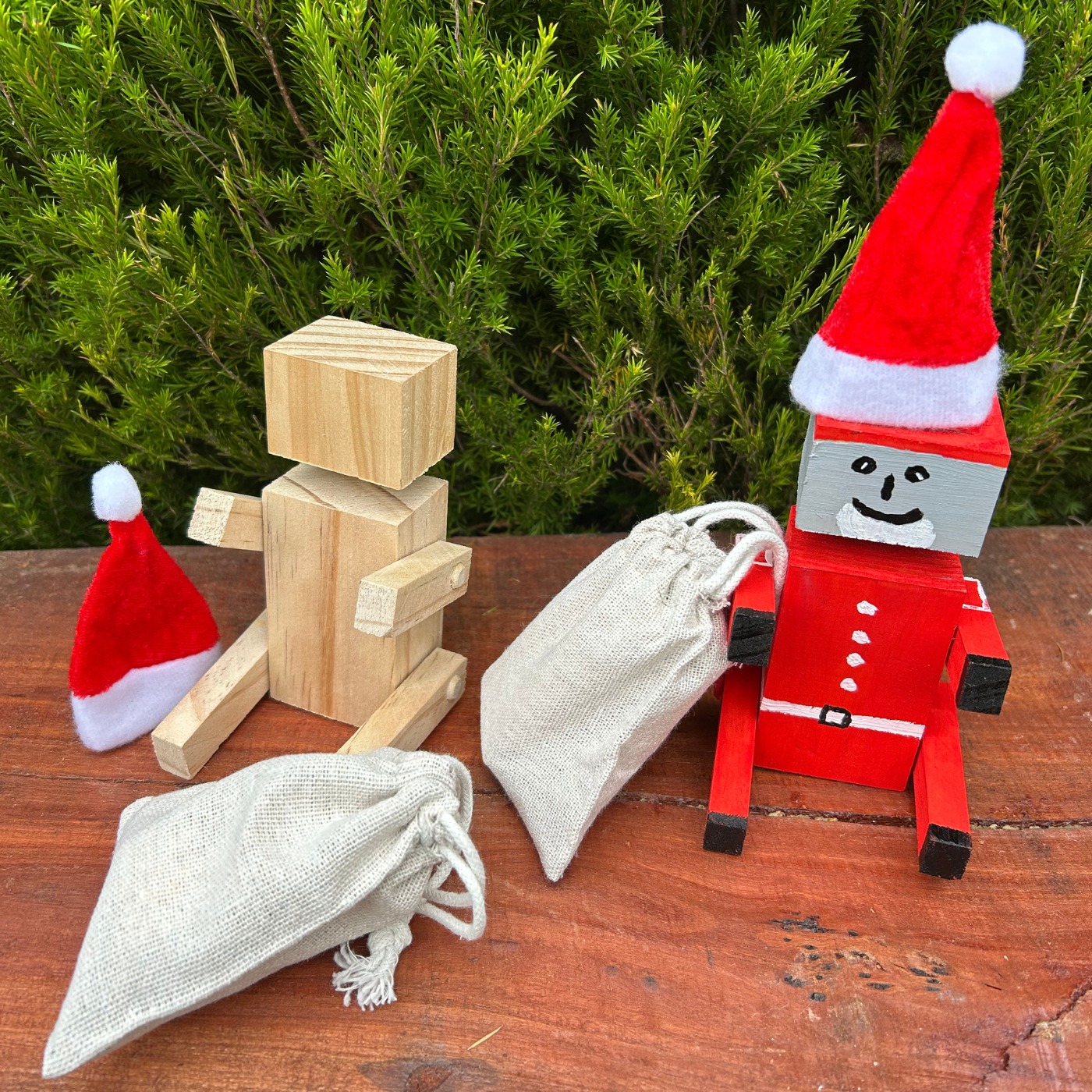 Wooden robot toys with Santa hats on a wooden surface with greenery in the background
