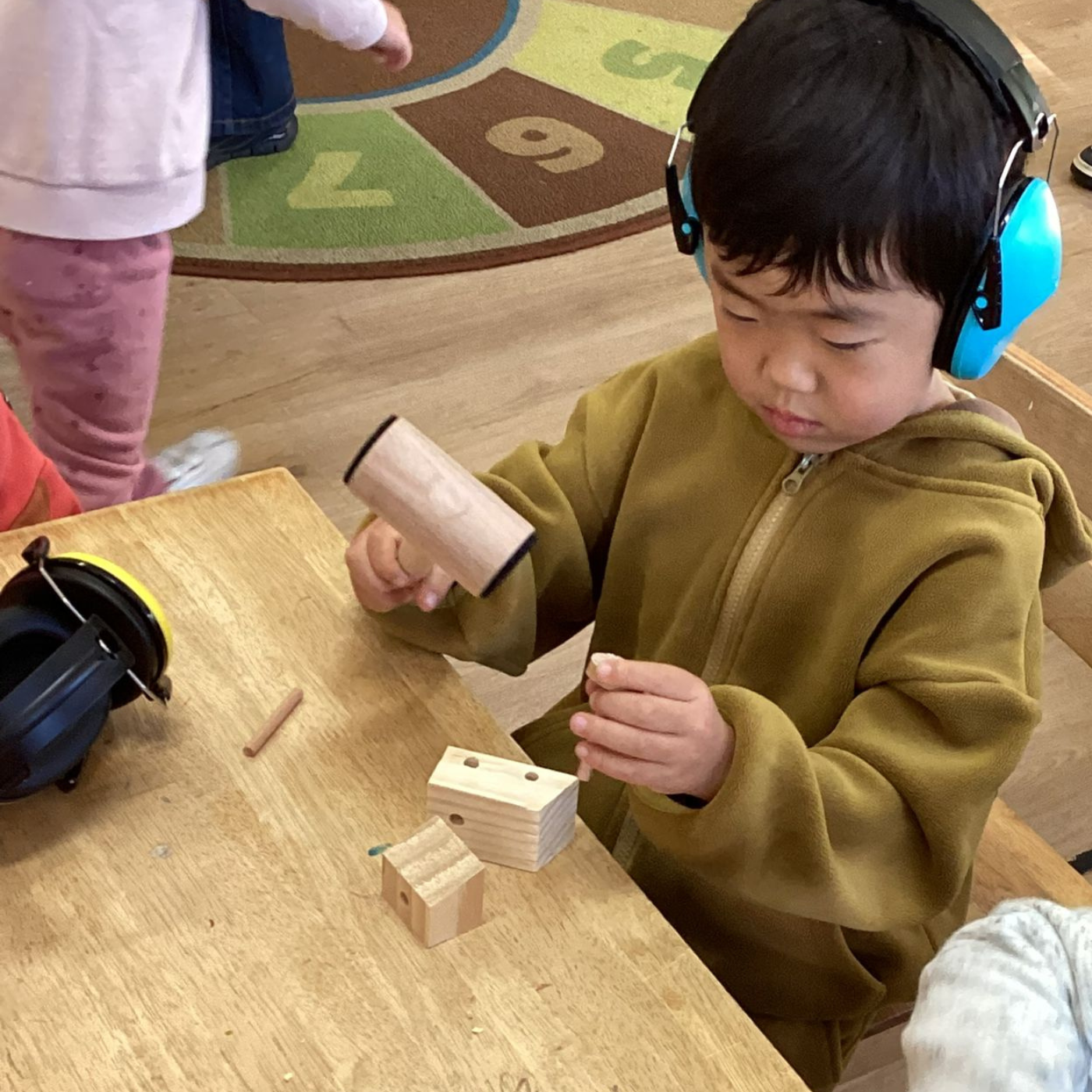 Child playing with wooden blocks at a table, wearing headphones.