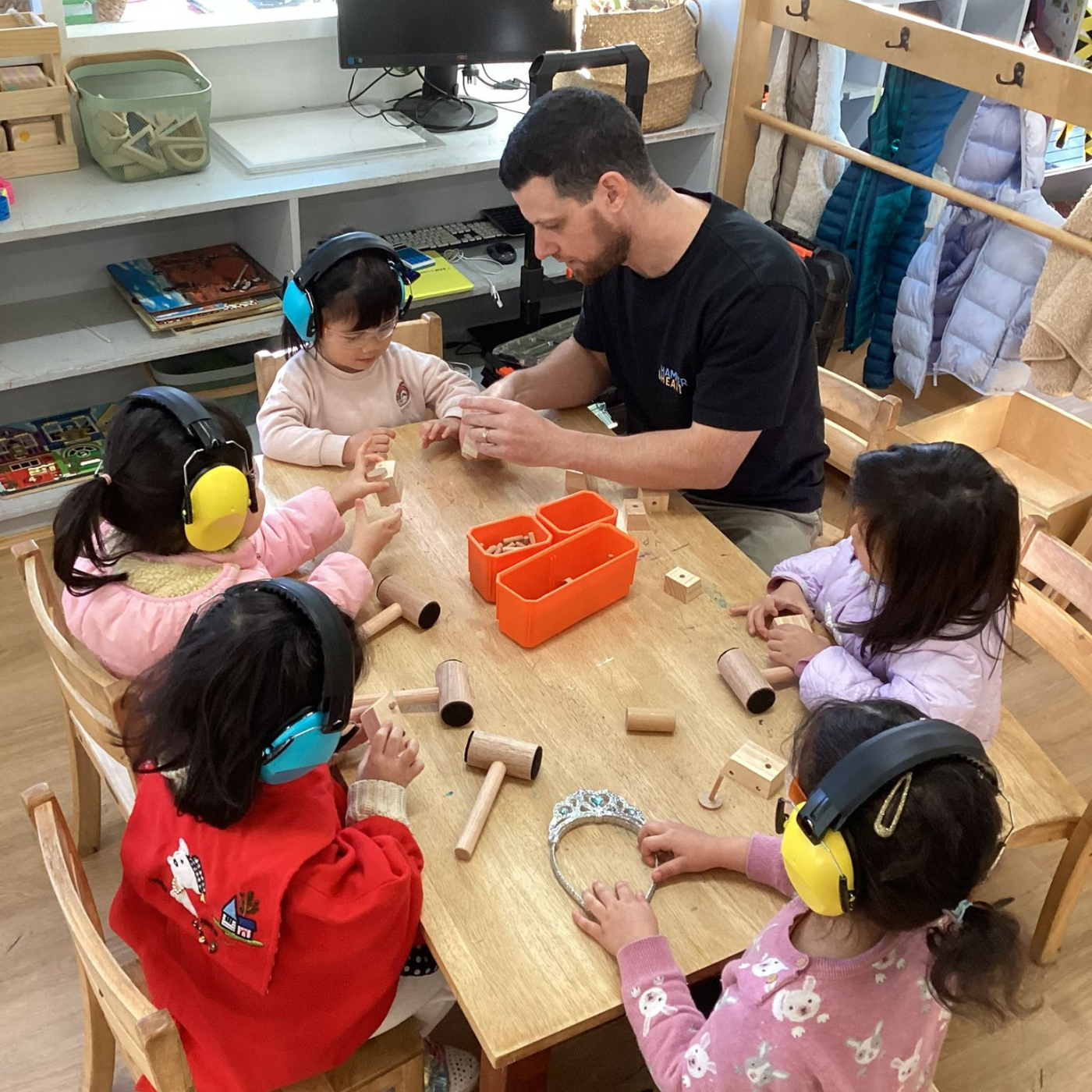 Children learning with wooden blocks at a table in a classroom setting with a teacher.
