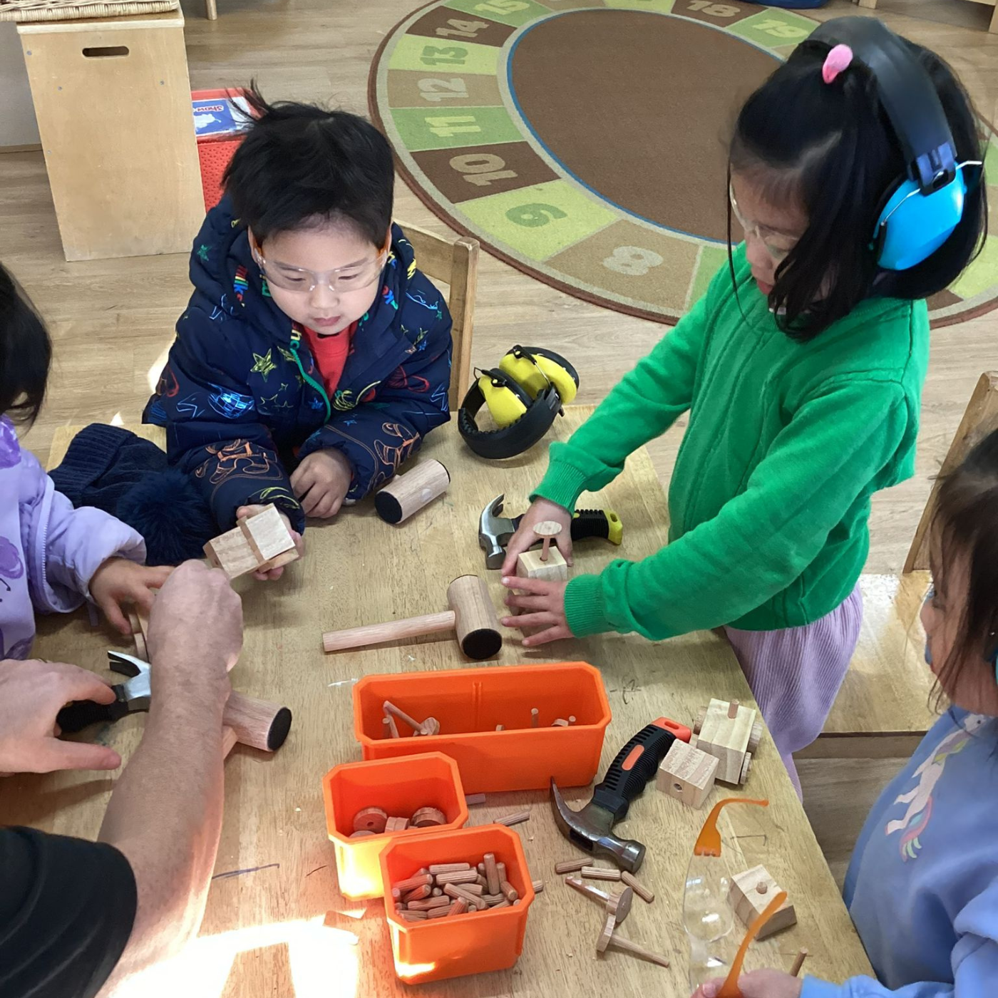 Children playing with tools and building blocks on a wooden floor.